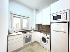 A modern kitchen with a built-in oven, microwave, and washing machine, a window with a view, and a sink. - Modern and bright apartment in the heart of Malaga (Málaga)