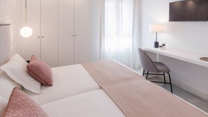 Habitación de hotel moderna con cama, escritorio y silla. Se observa un armario y un televisor montado en la pared.