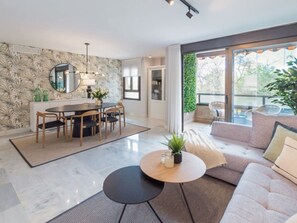 A modern living room with a dining area, a large window with a view of greenery, and a marble floor. - Premium Apartment with Terrace in Málaga (Málaga)