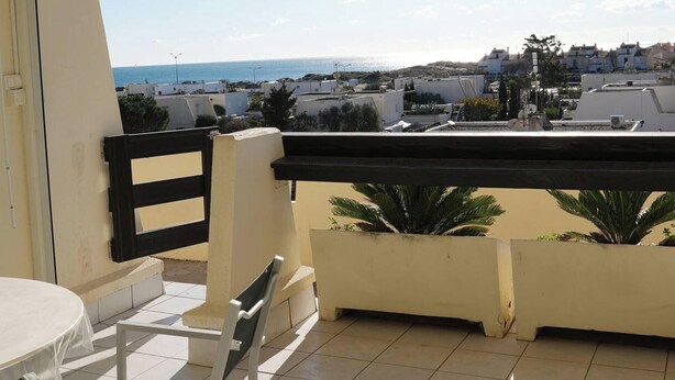 Varanda com vista para o mar e edifícios. Há uma mesa e uma cadeira.