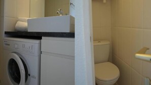 Casa de banho compacta com máquina de lavar, sanita e lavatório.