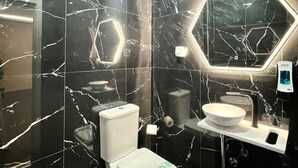 Ein modernes Badezimmer mit Marmorwänden, einem sechseckigen Spiegel, einer Toilette und einem Waschbecken.