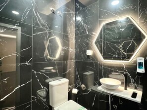 Ein modernes Badezimmer mit Marmorwänden, einem sechseckigen Spiegel, einer Toilette und einem Waschbecken.