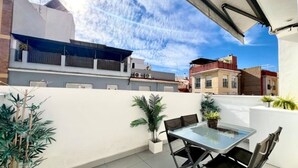 Eine Dachterrasse mit einem Glastisch und Stühlen, umgeben von Kübelpflanzen.