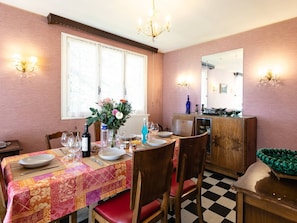 Un comedor con suelo a cuadros, una mesa dispuesta con platos, vasos y una botella, y un jarrón de flores.