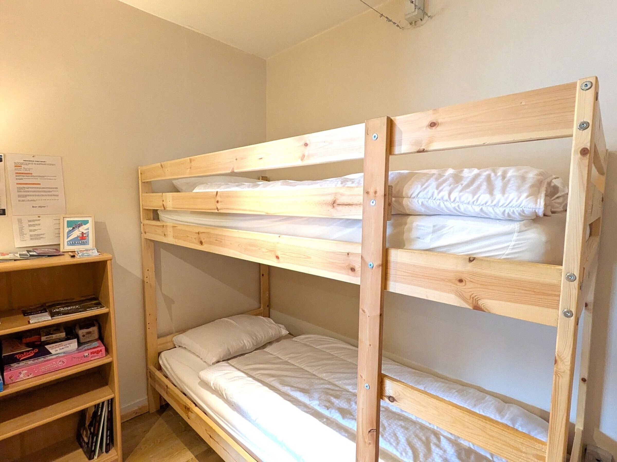 Ein Stockbett mit Holzrahmen, ein Regal mit Büchern und ein Poster an der Wand.