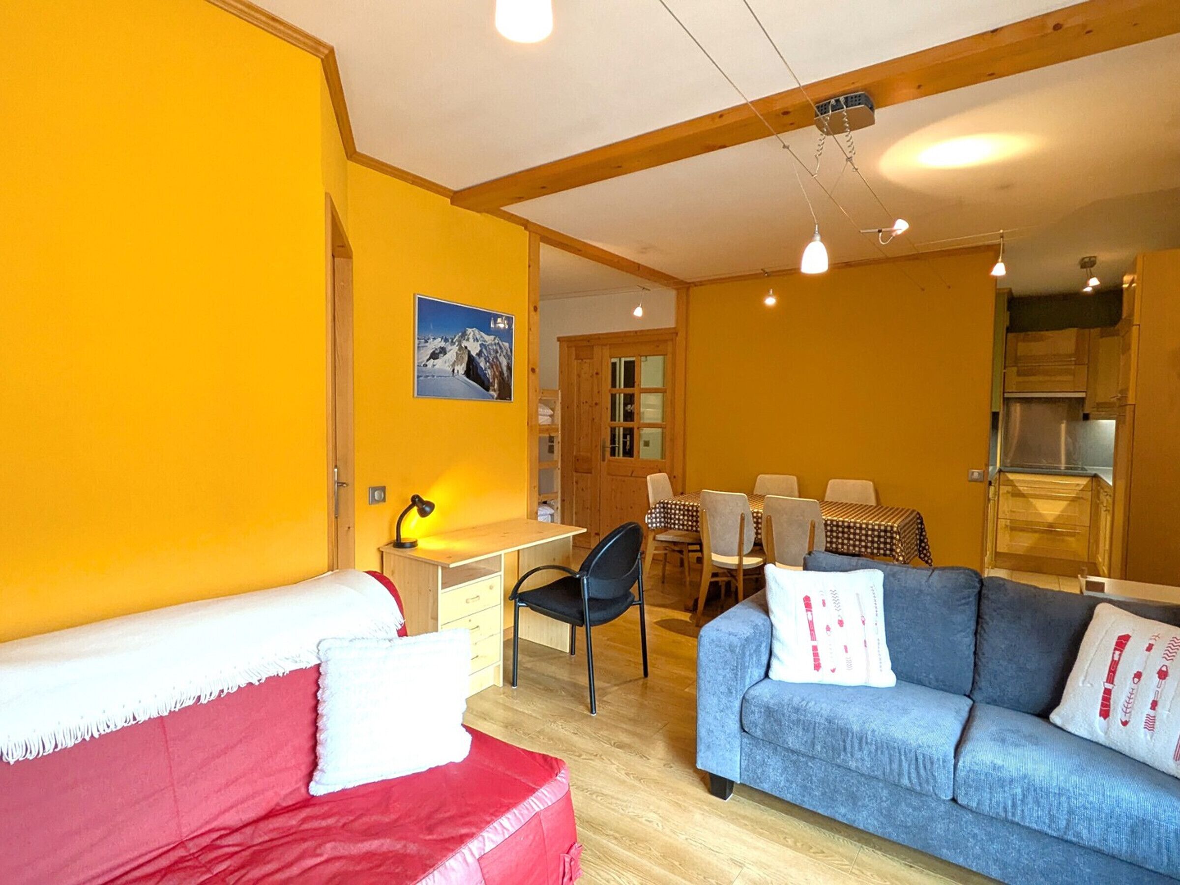 A room with a red sofa, a blue sofa, a wooden desk, and a dining table with chairs.