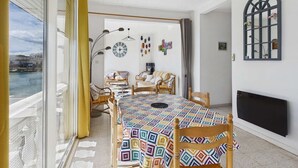 Ein Zimmer mit großem Fenster, einem Tisch mit bunten Tischdecken, Korbmöbeln und einer außergewöhnlichen Deckenleuchte.
