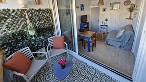Ein moderner Wohnraum mit einer Schiebeglastür, die auf einen Balkon führt, einem Essbereich mit Tisch und Stühlen, einer Couch und einem Fernseher im Hintergrund.