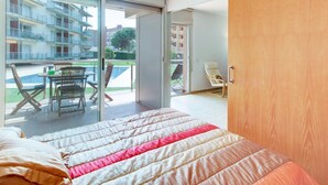 Een slaapkamer met een bed, een houten deur, een balkon met een tafel en stoelen, en uitzicht op gebouwen.