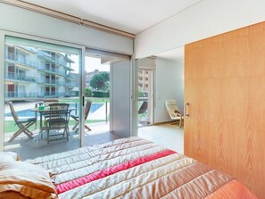 A bedroom with a bed, a wooden door, a balcony with a table and chairs, and a view of buildings. - Family Apartment with Parking and Air Conditioning in Roses (Roses)