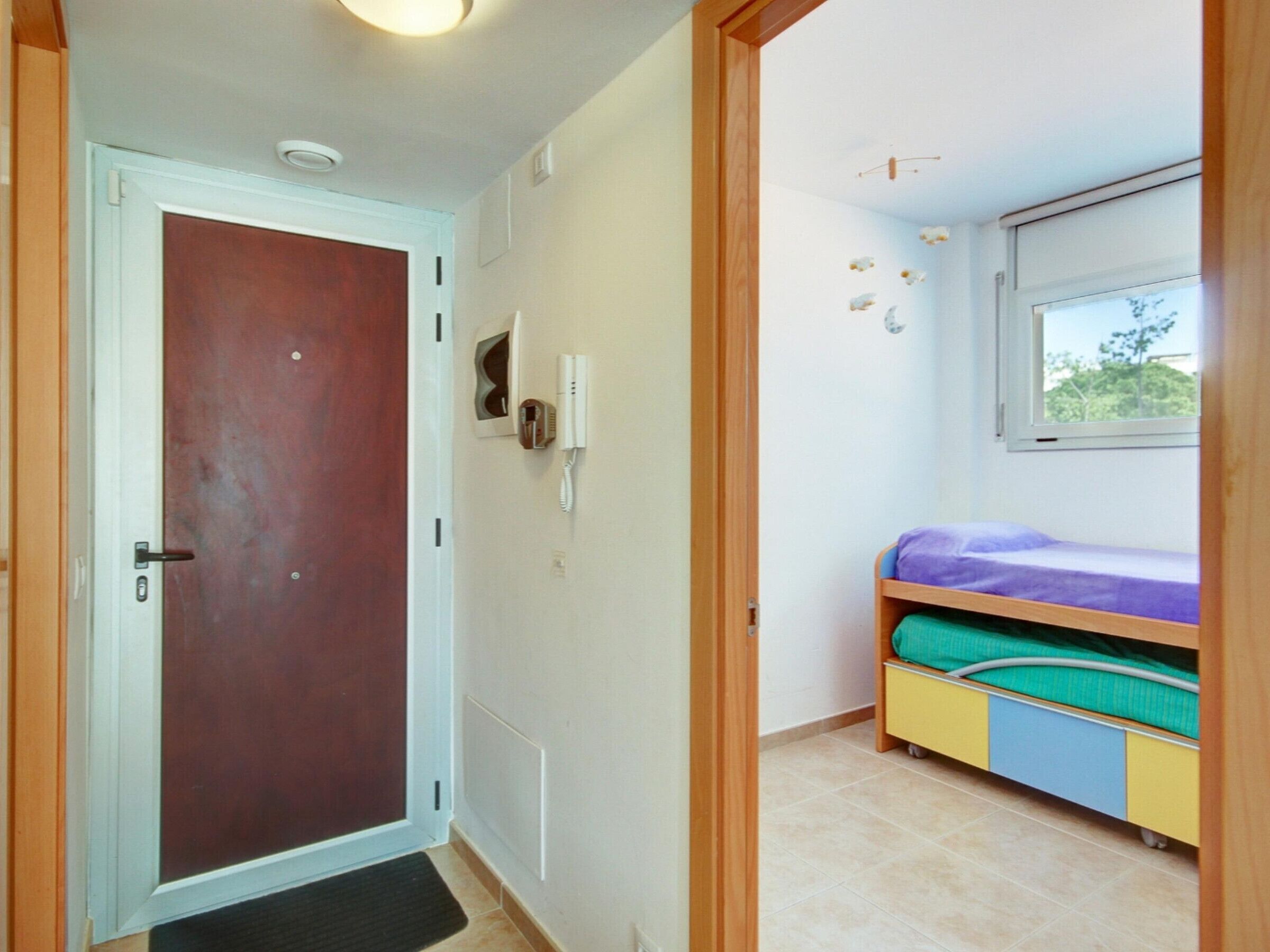 A room with a door, a wall-mounted phone, a window with a view, and a bunk bed with colorful bedding.