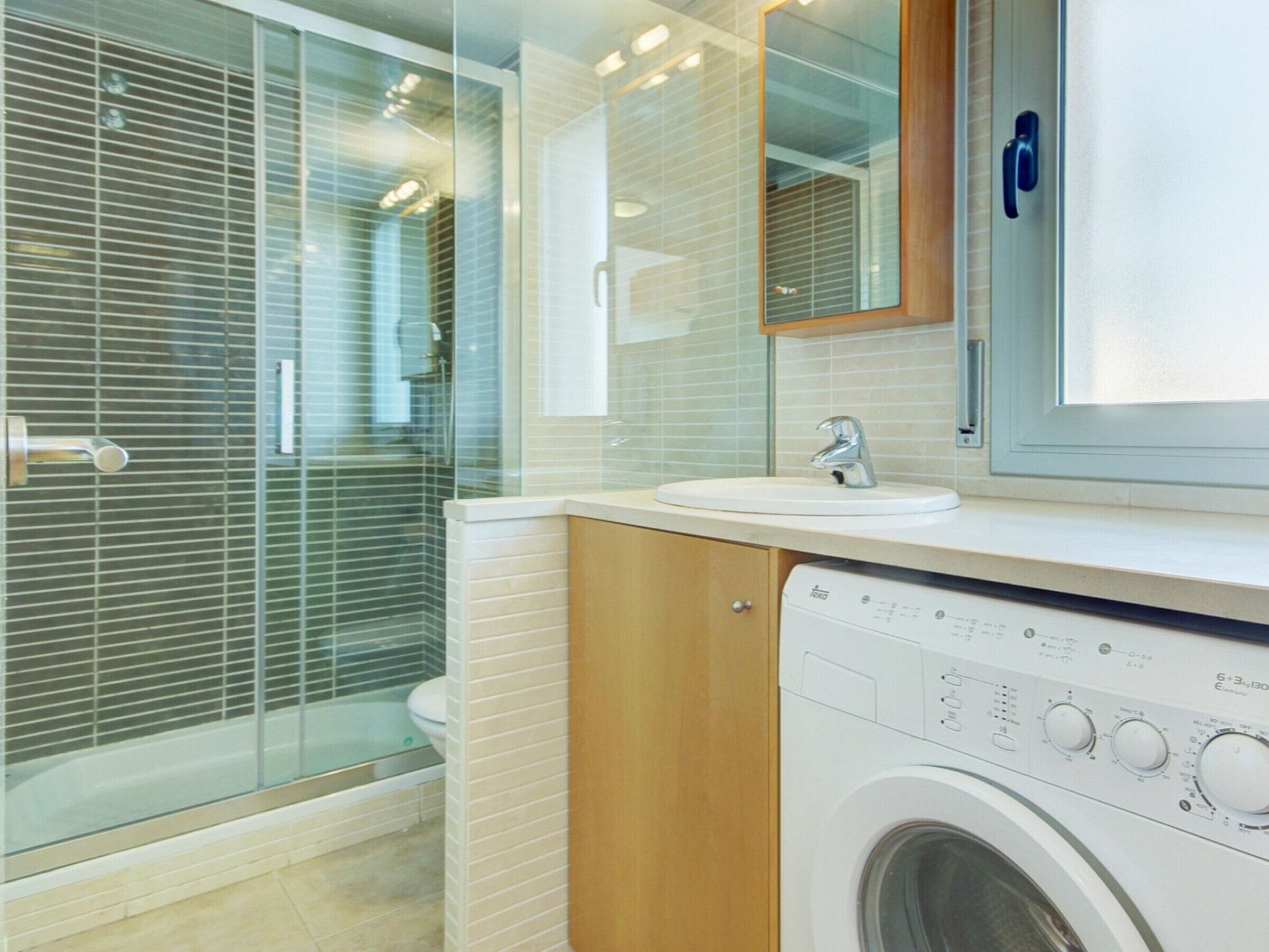 Un bagno moderno con box doccia in vetro, lavabo con specchio e una lavatrice a carica frontale.