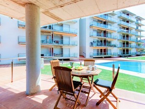 A poolside area with a table and chairs, a pool, and a multi-story building with balconies. - Family Apartment with Parking and Air Conditioning in Roses (Roses)