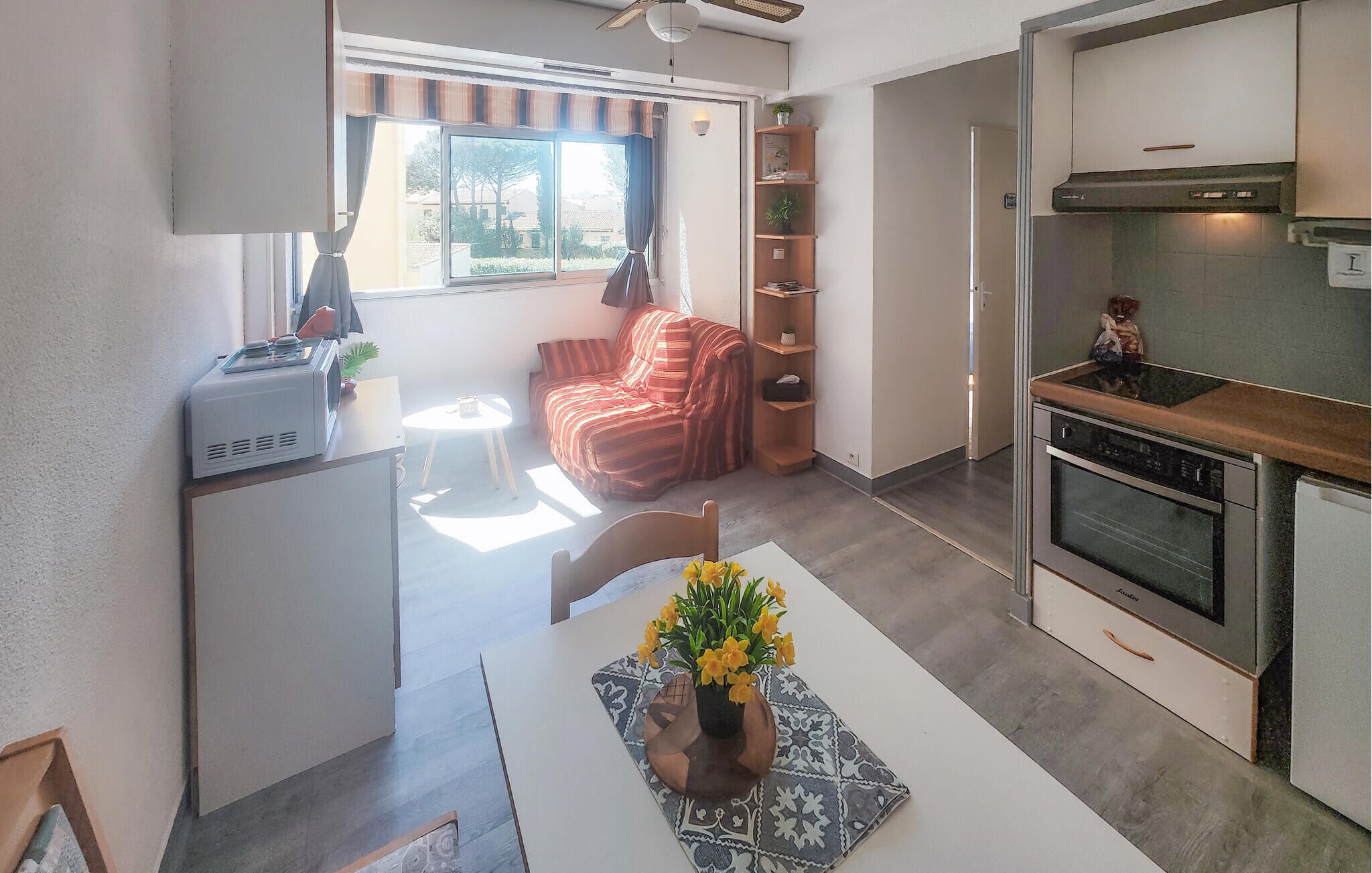 A compact living space with a kitchenette, a dining area with a table and chairs, a sofa, and a window with curtains.