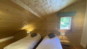 A small, cozy room with two single beds, wooden walls, a window with a view, and a nightstand with a lamp. - 4-Bedroom Duplex with Balcony and Parking in Valmorel (Valmorel)