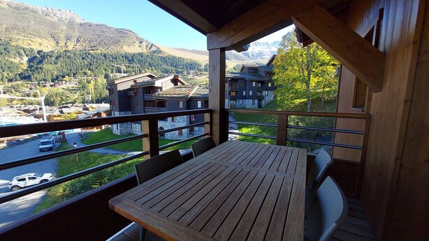 A wooden balcony with a table and chairs, overlooking a mountainous landscape with buildings and a road. - 4-Bedroom Duplex with Balcony and Parking in Valmorel (Valmorel)