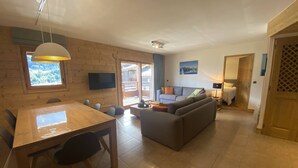 A spacious living area with a wooden dining table, a sofa, and a TV mounted on the wall. - 4-Bedroom Duplex with Balcony and Parking in Valmorel (Valmorel)