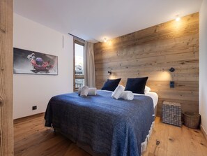 A bedroom with a wooden wall, a bed with a blue blanket, two pillows, and a painting on the wall. - Brand-new apartment in Lavachet, near slopes, sleeps 10 (Tignes)