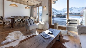 A spacious living area with a wooden ceiling, large windows with a mountain view, and a dining area with fur-covered chairs. - Brand-new apartment in Lavachet, near slopes, sleeps 10 (Tignes)