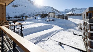 A snow-covered mountain landscape with modern buildings, including a multi-story structure with balconies, and a wooden deck overlooking the scene. - Brand-new apartment in Lavachet, near slopes, sleeps 10 (Tignes)