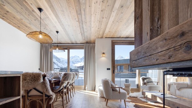 A cozy, rustic interior with wooden floors, a dining area with chairs, a fireplace, and a view of mountains through large windows. - Brand-new apartment in Lavachet, near slopes, sleeps 10 (Tignes)
