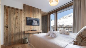A bedroom with a wooden wall, a TV, a bed with towels, and a view of a snowy mountain. - Brand-new apartment in Lavachet, near slopes, sleeps 10 (Tignes)