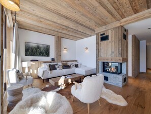 Ein modernes Wohnzimmer mit Kamin, Holzbalkendecke, einer Sofagarnitur und einem großen Gemälde an der Wand.