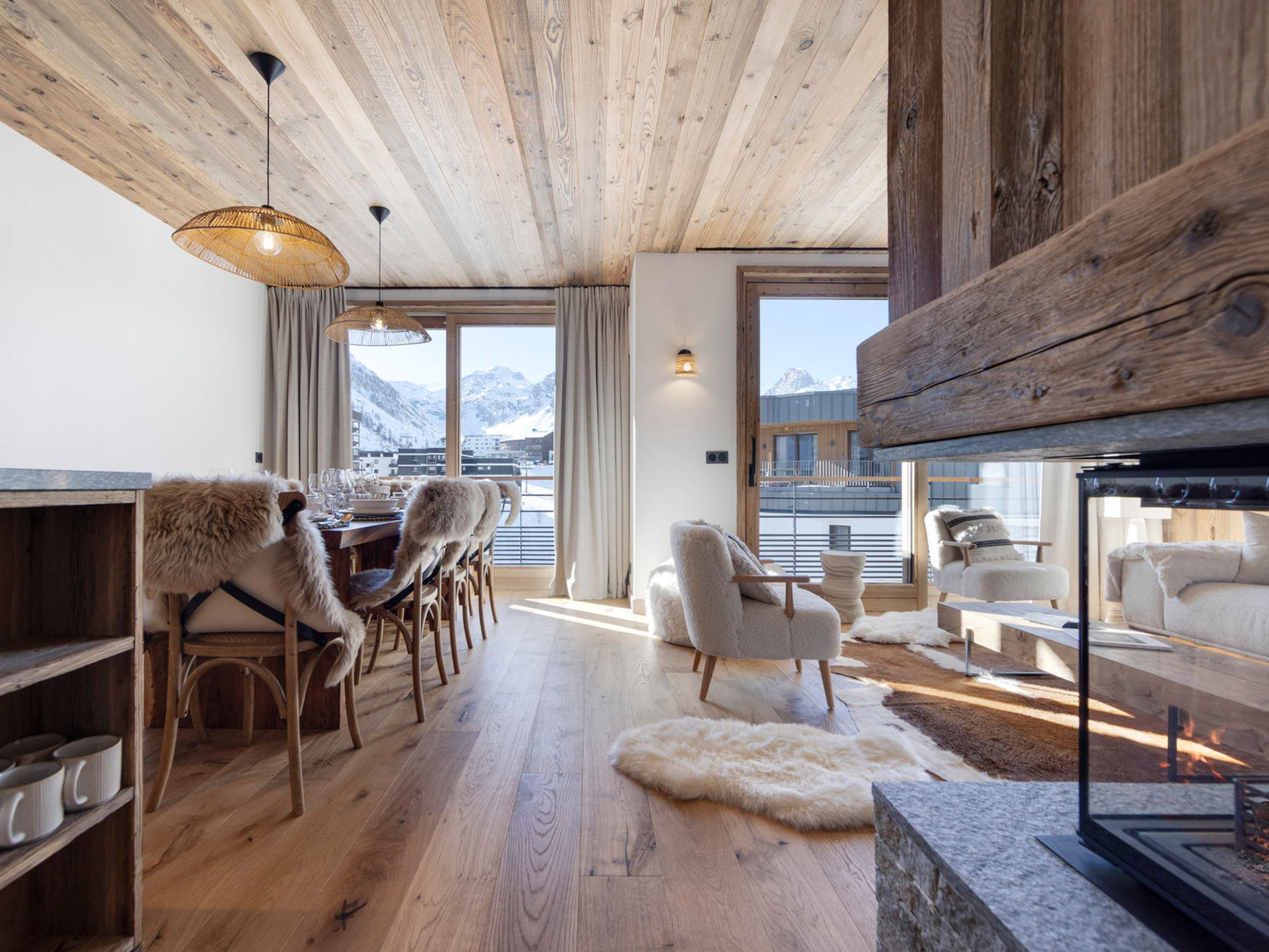 A cozy interior with a wooden ceiling, a dining area with chairs and a table, and a seating area with a fireplace.
