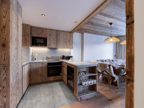 A modern kitchen with wooden cabinetry, a built-in oven, and a dining area with a fur-covered chair. - Brand-new apartment in Lavachet, near slopes, sleeps 10 (Tignes)