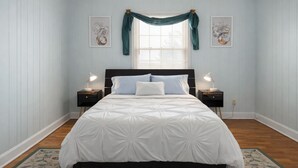 A bedroom with a large bed, two bedside tables with lamps, a window with curtains, and two framed pictures on the walls. - Cozy Comfort Home Frankfort, KY (Frankfort)