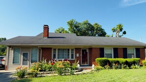 A single-story brick house with a gabled roof, a front porch, and a well-maintained front yard with various plants and a lawn. - Cozy Comfort Home Frankfort, KY (Frankfort)