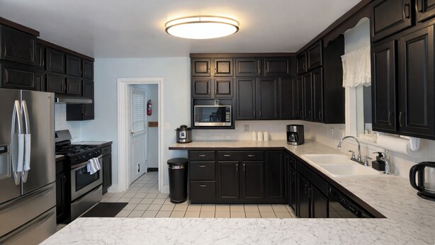 A modern kitchen with dark cabinetry, a stainless steel refrigerator, a microwave, a stove, and a sink. - Cozy Comfort Home Frankfort, KY (Frankfort)