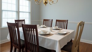 A dining room with a white table set for six, wooden chairs, a chandelier, and large windows with blinds. - Cozy Comfort Home Frankfort, KY (Frankfort)