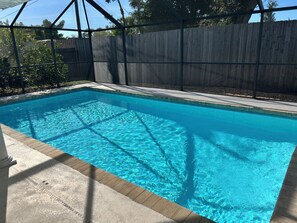 Ein rechteckiger Swimmingpool mit klarem, blauem Wasser, umgeben von einer Betonplattform und einem Holenzaun.