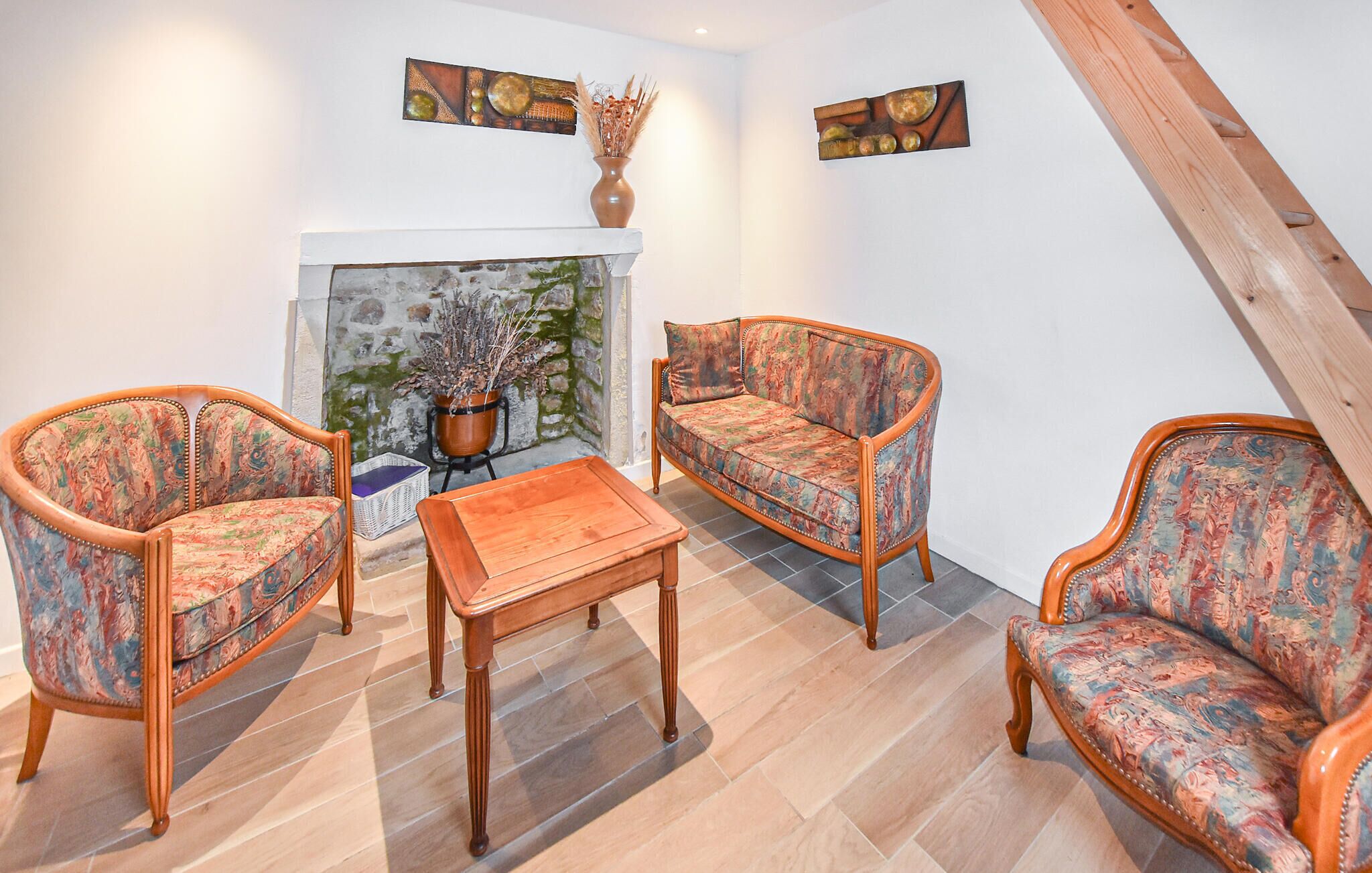 Un salon avec deux fauteuils à motifs, une table basse en bois et un canapé. On y trouve une cheminée avec un mur en pierre et une plante en pot.