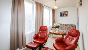Una habitación con dos sillones de cuero rojo, un sofá floral, una mesita con un jarrón y un cuadro en la pared.
