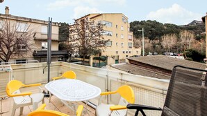 Una terraza con una mesa redonda y sillas amarillas y blancas, con vistas a un paisaje urbano que incluye edificios y una colina.