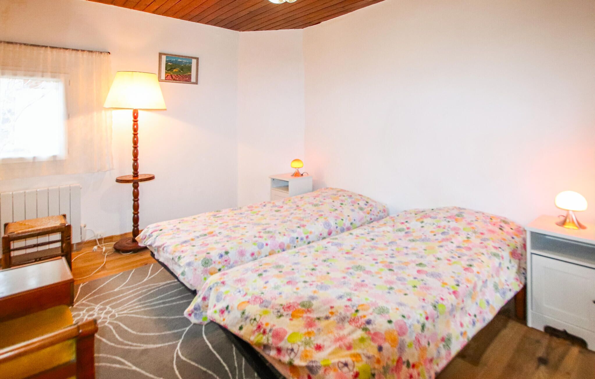 A bedroom with two beds, a desk, a chair, a lamp, and a radiator.
