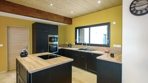 Een keuken met een centraal eiland, zwarte kastjes, een raam en een houten plafond.