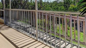 Ein Balkon mit Metallgeländer, Fliesenboden und Blick auf Bäume und Grün.