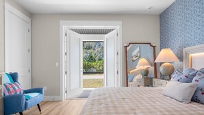Un dormitorio con una cama grande, una silla, un tocador y un espejo. Hay una puerta que da a un espacio exterior.