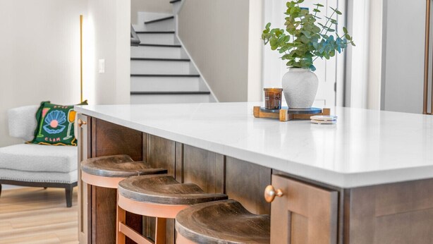 Una cocina con encimera blanca, taburetes de madera y una planta en la encimera.