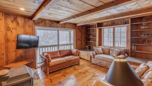 Interior acogedor de una cabaña con paredes de madera, chimenea, sofás de cuero y televisor.