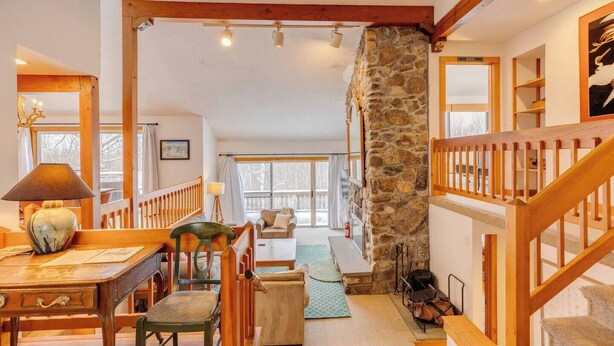 Un interior acogedor con una escalera de madera, una pared de piedra y una zona de estar con vistas al exterior.