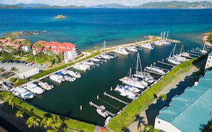 Luftaufnahme einer Marina mit mehreren angossenen Booten, umgeben von Gebäuden mit roten Dächern und Palmen.