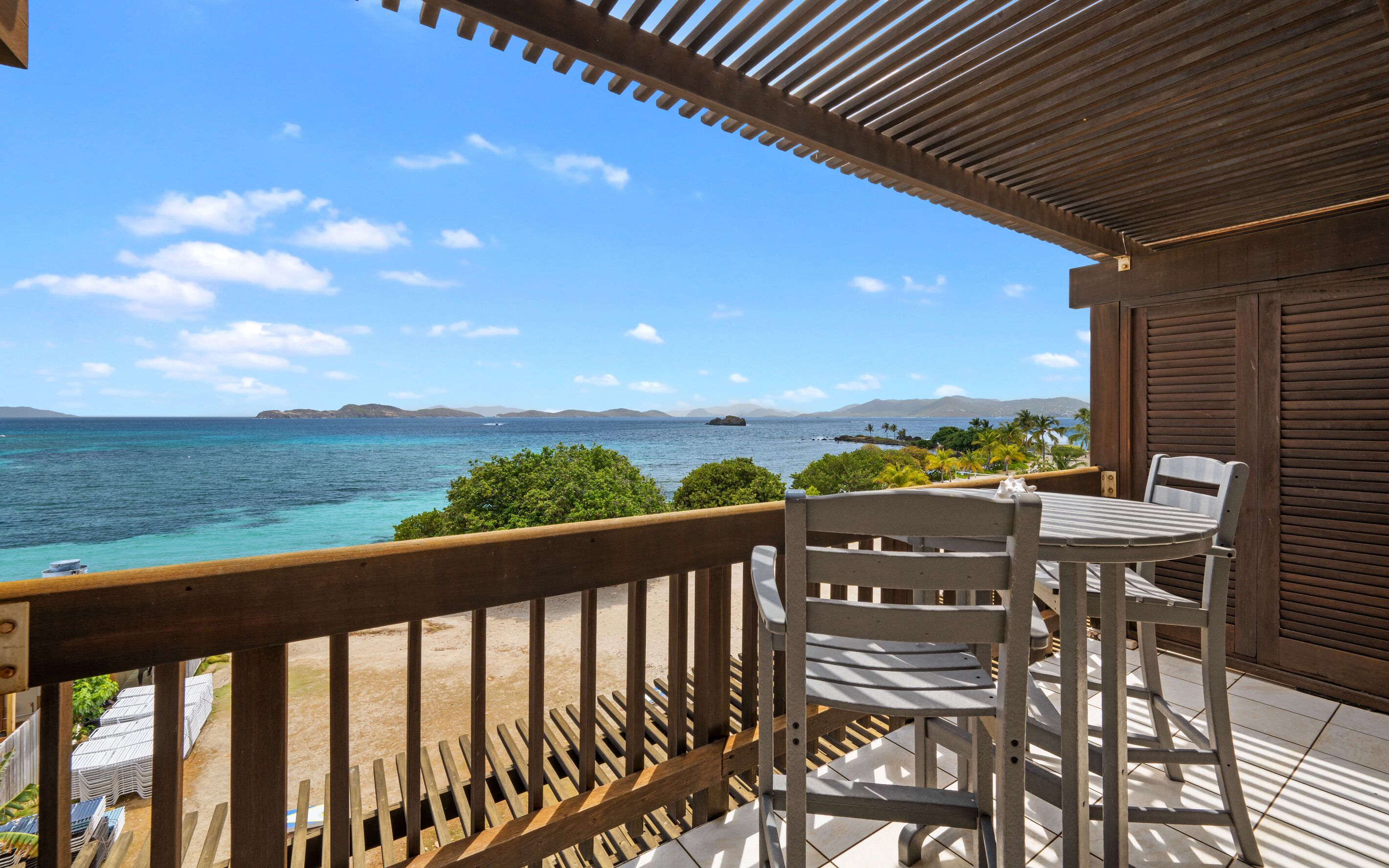 A balcony with a view of the sea, a table, and chairs.