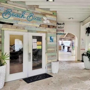 Une entrée sur le thème de la plage, avec une façade en bois, un bar bien visible et un chemin d’accès dégagé menant à l’intérieur.