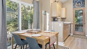 A dining area with a table set for four, a kitchen with wooden cabinets, and a view of trees through large windows. - Latitude 45 - forest retreat near Manzanita beach (Manzanita)