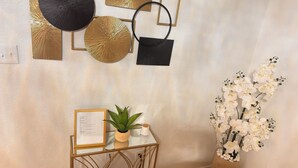 A room with a white textured wall, a small table with a plant and a framed document, and a vase with white flowers. - Your Arlington Hotspot: Games, Flights & Family Fun (Arlington)
